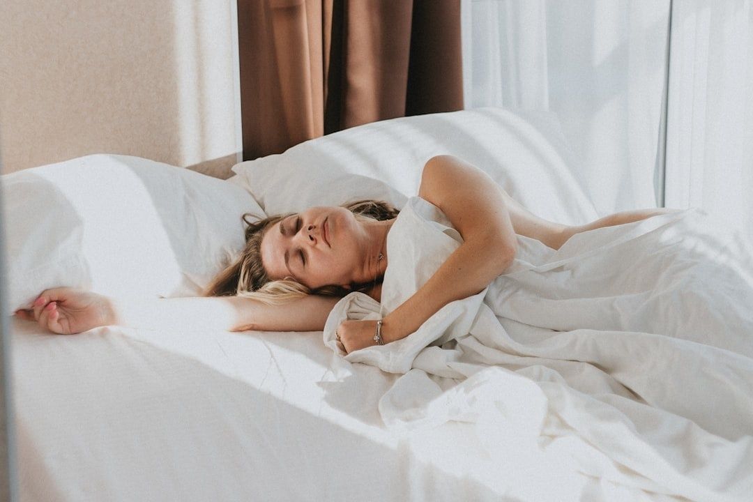 Kvinna sover utsträckt i en ljus säng med vita lakan